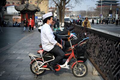 A chef sitting on an electric bike makes a phone call in Beijing on March 8, 2021. (Photo by GREG BAKER / AFP)