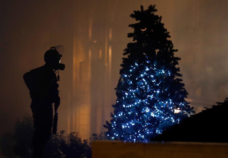 A riot police officer stands next of a Christmas tree during a protest. AP