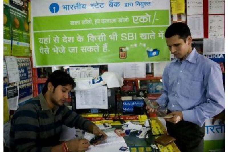 A shopkeeper transfers money for customers using text commands on a mobile phone in New Delhi. Manpreet Romana / AFP