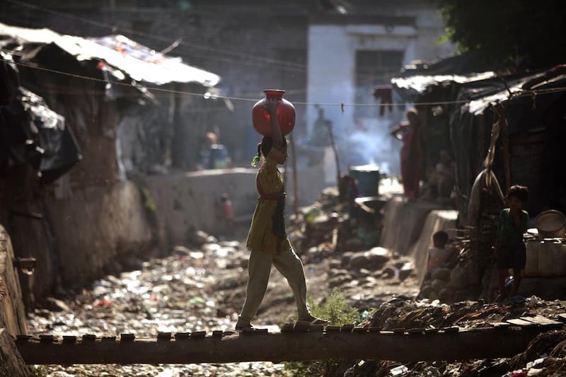 A young Indian girl walks back home carrying a canister of drinking water over her head filled from a public tap, in a shanty town on the outskirts of Jammu, India. Channi Anand / AP