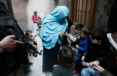 A policeman guards a health worker as she gives a polio vaccination to a child in Peshawar, Pakistan, Monday, Dec. 16, 2019. Pakistan government launched a nationwide anti-polio vaccination campaign in an effort to eradicate the crippling disease as the total number of affected children rose to over 100 in 2019, an official said. (AP Photo/Muhammad Sajjad)