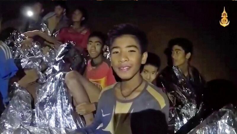 FILE - In this July 3, 2018, file image taken from video provided by the Royal Thai Navy Facebook Page, the boys smile as Thai Navy SEAL medic help injured children inside a cave in Mae Sai, northern Thailand. The group was discovered July 2 after 10 days totally cut off from the outside world, and while they are for the most physically healthy, experts say the ordeal has likely taken a mental toll that could worsen the longer the situation lasts. (Royal Thai Navy Facebook Page via AP, File)