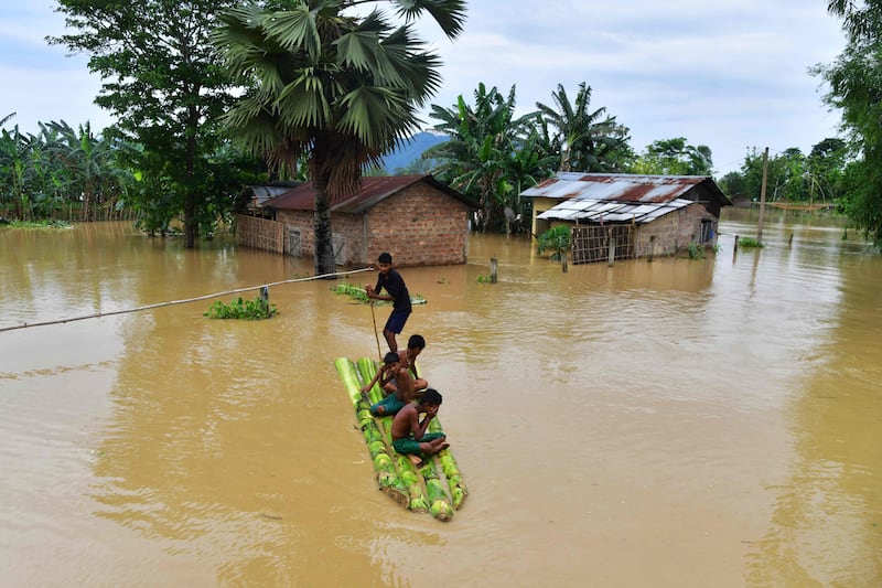 Children make their way on a raft past homes in a flooded area. AFP