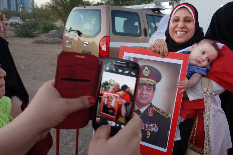 Ganaa holds her baby Yossef in a long line of voters at the Egyptian embassy, while also holding a poster of Abdel Fattah El Sisi. Delores Johnson / The National