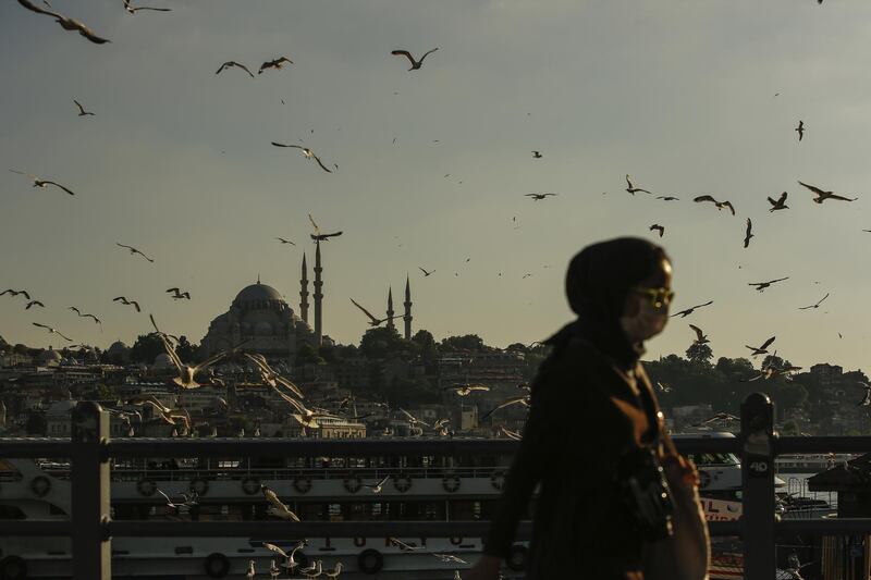 A woman walks as seagulls fly over a boat on the Bosphorus Strait separating Europe and Asia, in Istanbul. AP Photo