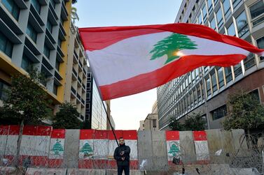 An anti-government protester waves a national flag in front of a concrete wall set up by Lebanese police to block a road leading to the parliament building in downtown Beirut, Lebanon. EPA