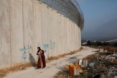 A Palestinian woman walks alongside the Israeli separation barrier to harvest olives in the West Bank village of Beit Awwa, south-west of Hebron. AFP  