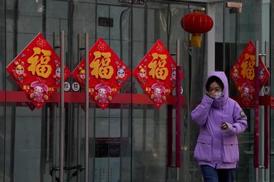 A woman adjusts her mask near decorations set up ahead of the coming Chinese Lunar New Year in Beijing. AP