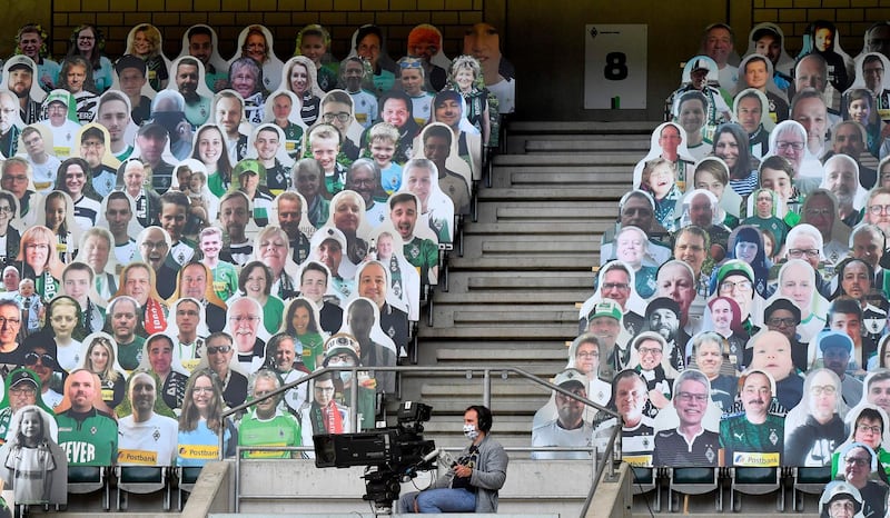 A TV camera operator wears a face protection mask, surrounded by cardboards with photos of Moenchengladbach fans on the stands. AFP