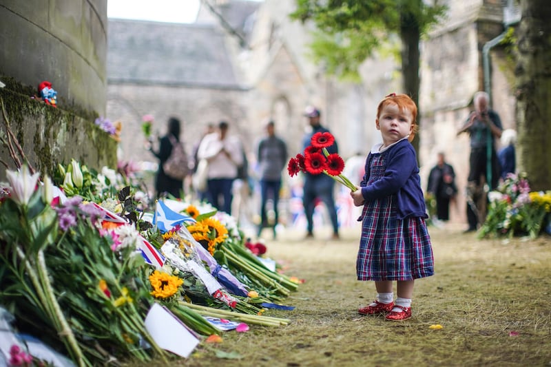 A child lays flowers in remembrance of Queen Elizabeth outside the Palace of Holyroodhouse in Edinburgh. AP