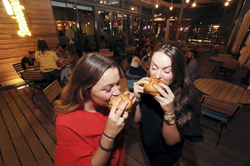 Dubai, United Arab Emirates - September 10, 2018: Louise Desfrenne (L) takes a bite out of the new vegan burger while Annie Turnell takes a bite out of a beef burger. Bareburger are launching a revolutionary plant-based (vegan) burger that looks, cooks and satisfies like beef. Monday, September 10th, 2018 at La Mer, Dubai. Chris Whiteoak / The National