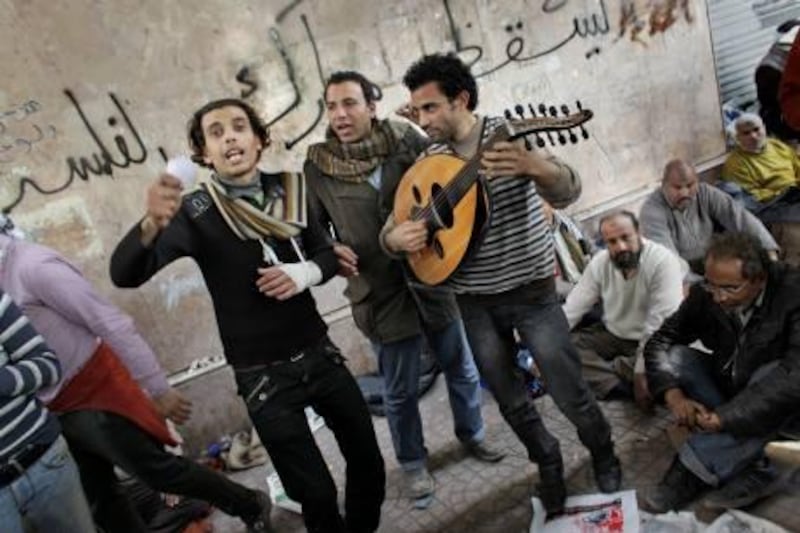 A group of musicians, one playing the Oud, center-right, entertain anti-government protesters with songs against Egyptian President Hosni Mubarak at the continuing demonstration in Tahrir square in downtown Cairo, Egypt Friday, Feb. 4, 2011. Tens of thousands packed central Cairo Friday, waving flags and singing the national anthem, emboldened in their campaign to oust President Hosni Mubarak after they repelled pro-regime attackers in two days of bloody street battles. Graffiti in arabic on wall behind reads "Down Mubarak the corrupt". (AP Photo/Ben Curtis) *** Local Caption ***  ABC109_Mideast_Egypt.jpg