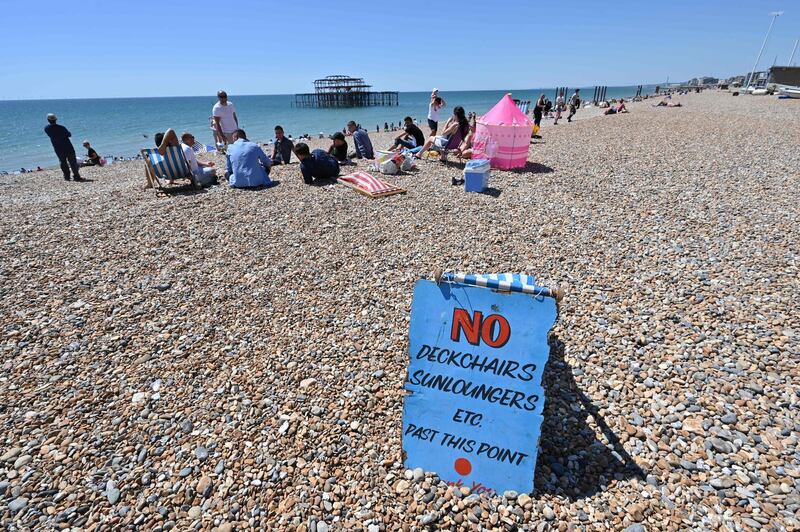 People sunbathe on the beach in front of the derelict West Pier in Brighton.  AFP