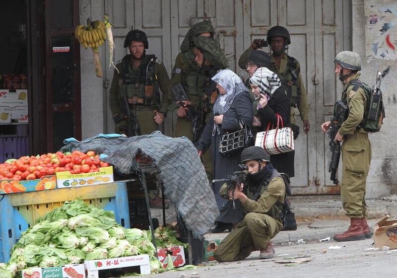 Palestinian women walk past Israeli security forces during clashes with Palestinian stone throwers in the West Bank city of Hebron. Hazem Bader / AFP 