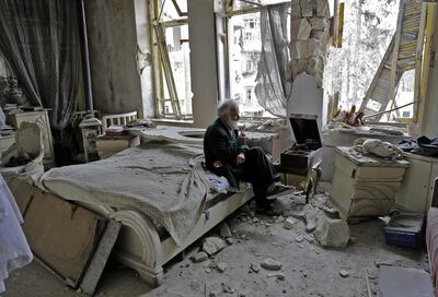 Mohammed Mohiedin Anis, or Abu Omar, 70, smokes his pipe as he sits in his destroyed bedroom listening to music on his vinyl player, gramophone, in Aleppo's formerly rebel-held al-Shaar neighbourhood. (Photo by JOSEPH EID / AFP)