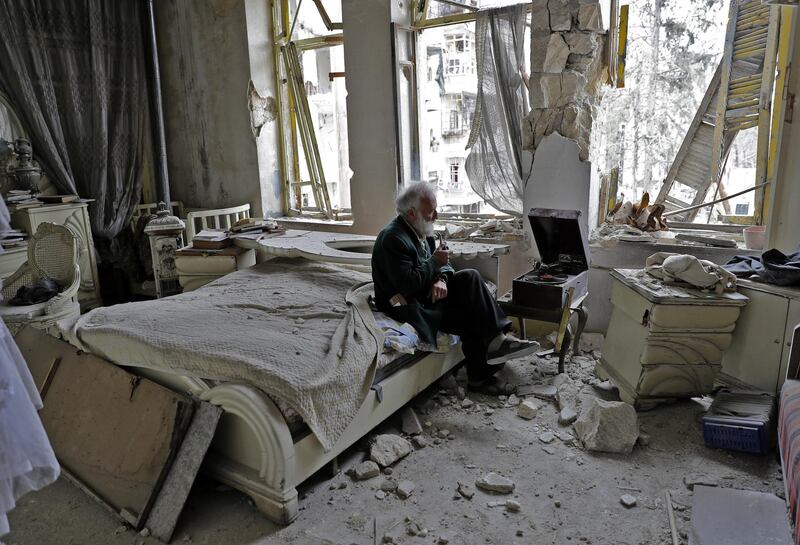 Mohammed Mohiedin Anis, or Abu Omar, 70, smokes his pipe as he sits in his destroyed bedroom listening to music on his vinyl player, gramophone, in Aleppo's formerly rebel-held al-Shaar neighbourhood. (Photo by JOSEPH EID / AFP)