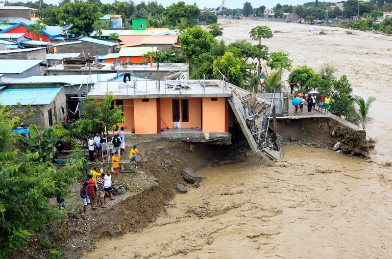 People stand near a damaged house hit by flood water on a river bank in Dili, East Timor. Dozens of people are dead or missing as floods and landslides caused by torrential rains hit the eastern part of Indonesia and East Timor.  EPA