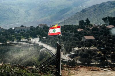 This picture taken on February 15, 2021 shows (foreground) flags of Lebanon and Lebanese Shiite movement Hezbollah (yellow) flying in Lebanon's southern plain of Marjayoun along the border with the northern Israeli town of Metulla (R).  / AFP / Mahmoud ZAYYAT

