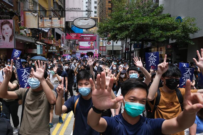 Demonstrators gesture the "Five demands, not one less" protest motto during a protest against a planned national security law in the Causeway Bay district in Hong Kong, China, on Sunday, May 24, 2020. Hong Kong police deployed a water cannon and fired tear gas as violence returned to the city's streets with hundreds of protesters marching against China's plans to impose a sweeping national security law. Photographer: Roy Liu/Bloomberg