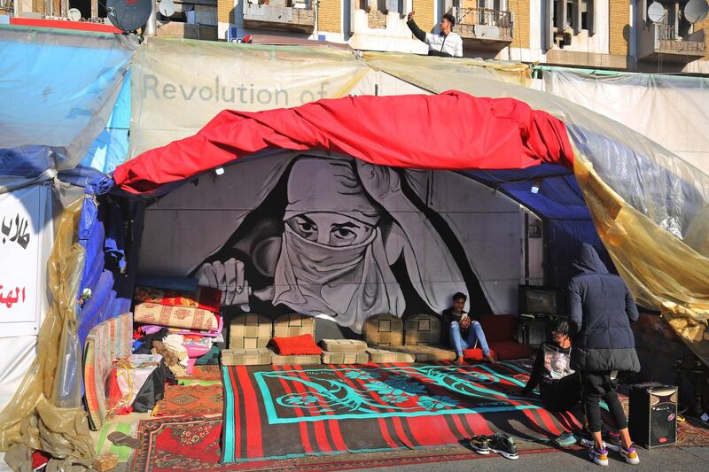 Iraqi anti-government protesters sit in a tent by murals inspired by ongoing demonstrations in the capital Baghdad's Tahrir square on January 14, 2020. AFP