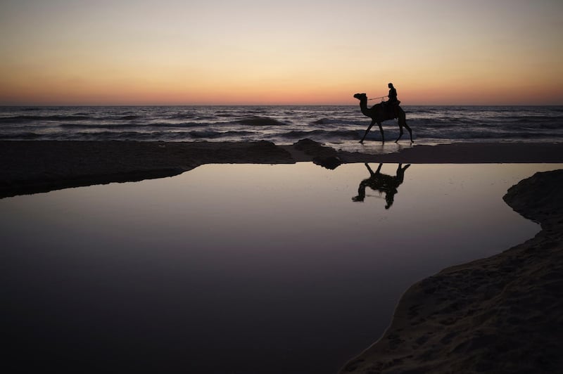 A Palestinian man rides his camel after sunset on the shores of the Mediterranean Sea, at the beach in Gaza City, Sunday, June 6, 2021. AP
