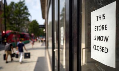 Pedestrians carry shopping bags as they walk past a sign in the window of a store alerting customers that the shop has closed-down, in London on August 12, 2020. Britain's economy contracted by a record 20.4 percent in the second quarter with the country in lockdown over the novel coronavirus pandemic, official data showed Wednesday.  "It is clear that the UK is in the largest recession on record," the Office for National Statistics said. Britain officially entered recession in the second quarter after gross domestic product (GDP) contracted by 2.2 percent in the first three months of the year. / AFP / Tolga AKMEN
