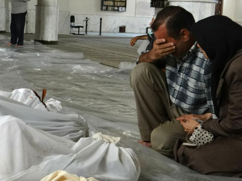 A Syrian couple mourns in front of bodies wrapped in shrouds before funerals after a chemical attack in Eastern Ghouta, on August 21, 2013. AFP