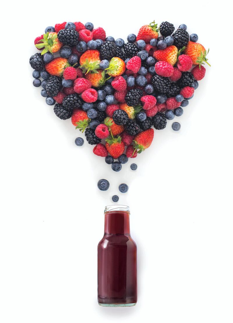 Assorted berry fruits flowing out from juice bottle, form into heart shape.