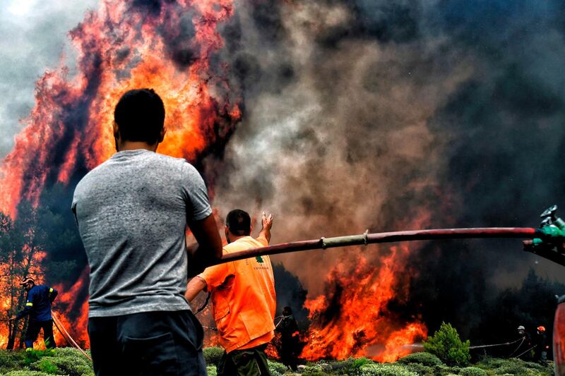 Firefighters and volunteers try to extinguish flames during a wildfire at the village of Kineta. AFP