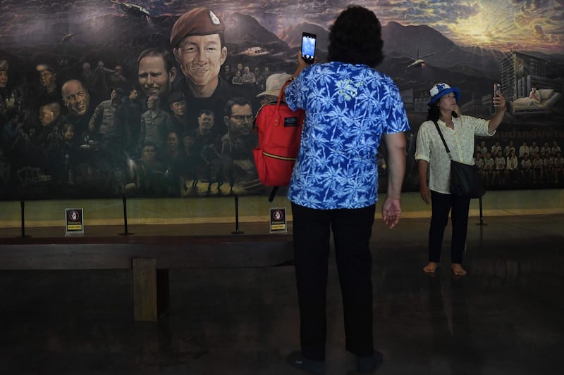 Visitors taking photos in front of a mural, illustrating the rescue of the 12 boys and their coach. AFP