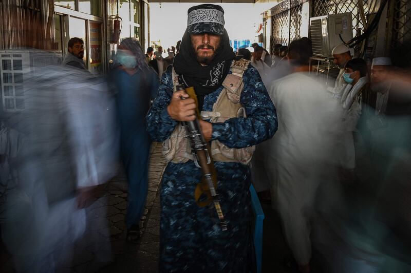 A Taliban fighter stands guard as people move past him at a market with shops dealing in foreign currency, in Kabul. AFP