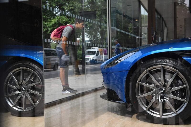 A pedestrian looks at an Aston Martin DB11 in a showroom in central London on August 29, 2018. - Aston Martin said today it plans to float one quarter of the British company on the London stock market, as demand rises worldwide for the luxury brand's cars favoured by fictional spy James Bond. (Photo by BEN STANSALL / AFP)