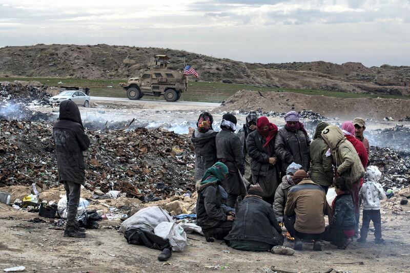A US army vehicle drives past as Syrians sift through a garbage dump in the countryside of Malikiya in northeast Syria, on January 17, 2021. - On the dry plains outside the city of Al-Malikiyah, a dozen people wrapped up against the cold rip open the black plastic bags, in a desperate search for something to sell, repurpose or even eat. Across the road, an oil pump swings back and forth in this resource-rich region controlled by US-backed Kurdish forces. (Photo by Delil SOULEIMAN / AFP)