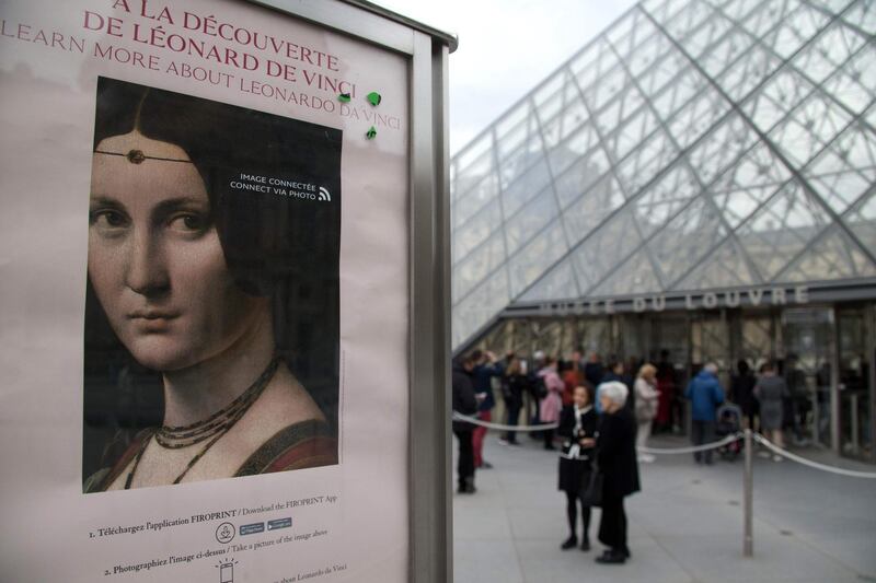 A poster for the exhibition 'Leonardo da Vinci' is seen in front of The Louvre Museum in Paris as visitors queue on the day of the exhibition's opening. AFP
