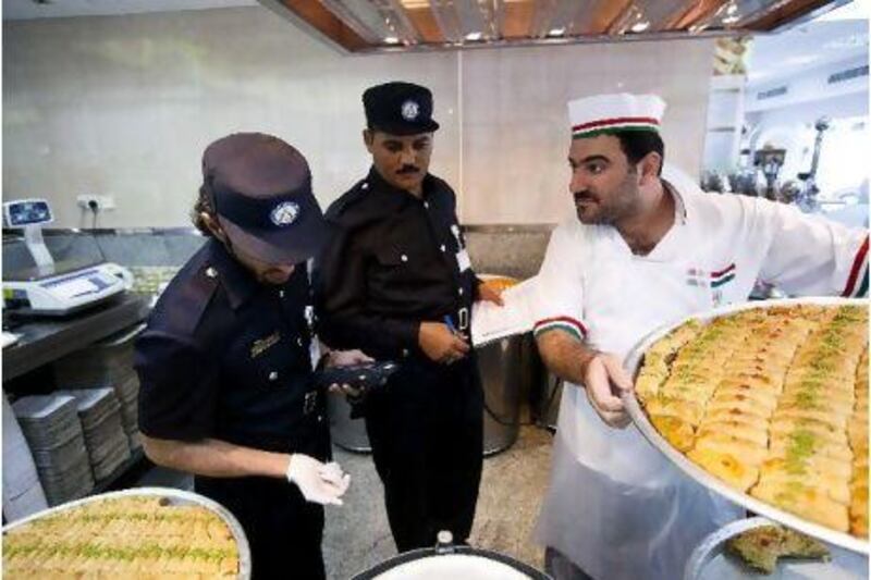 Omar Al Hussaini, left, and Mansour Adb El Latif, of the Abu Dhabi Food Control Authority, check produce and trays with Bashar Abdullah Al Ismail, the pastry head of Qaider Al Nabulsi Sweets.