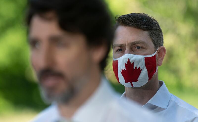 In this photo taken on June 19, 2020, Liberal Member of Parliament William Amos wears a Canadian flag mask as Prime Minister Justin Trudeau speaks during a news conference in Chelsea, Quebec. Amos, who has represented the Quebec district of Pontiac since 2015, appeared on the screens of his fellow lawmakers completely naked on Wednesday, April 14, 2021. He has apologized to his colleagues and says his video was accidentally turned on as he was changing into his work clothes after going for a jog. (Adrian Wyld/The Canadian Press via AP)