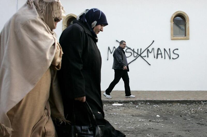 Muslim residents in France walk past racial slurs painted on the walls of a mosque in the town of Saint-Etienne. Laurent Cipriani / AP