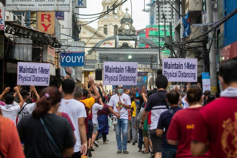 A church worker carries a placard reminding mass-goers to maintain physical distancing outside Quiapo Church in Manila, Philippines. Reuters