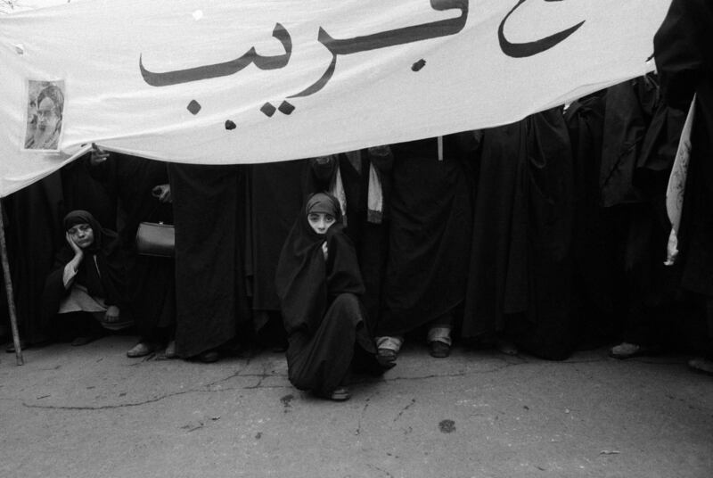 Women demonstrators, among them a young girl wearing a black chador (traditional Iranian cloak), sit under a banner with a photo of Ayatollah Khomeini in Revolution Square, on December 11, 1978. Getty Images