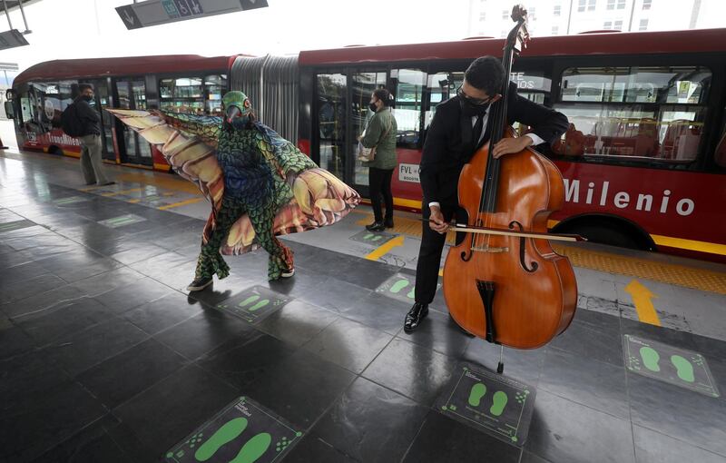 A musician from Bogota's Youth Philharmonic Orchestra plays a double bass as a person in a hummingbird costume promotes social distancing with her wings during their performance for commuters at a bus stop in Bogota, Colombia.  AP