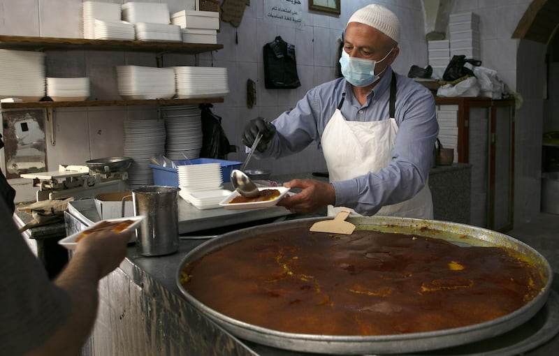 A Palestinian wearing a protective face mask sells knefeh (traditional Middle Eastern dessert) in the oldest knefeh store in the occupied West Bank city of Nablus.   AFP