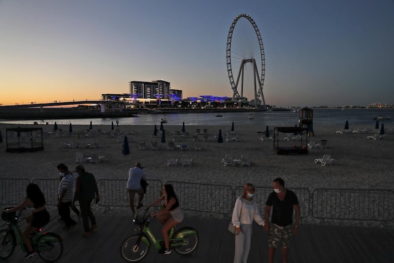 Tourists and residents enjoy the sunset at Jumeirah Beach Residence, with the Dubai Eye on Bluewaters Island in the background