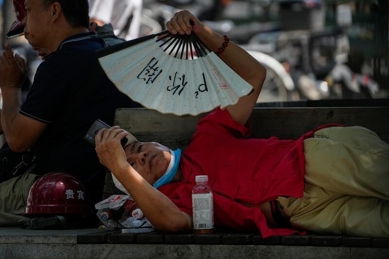 A man cools himself with a fan while browsing his phone on a sweltering day in Beijing. AP 