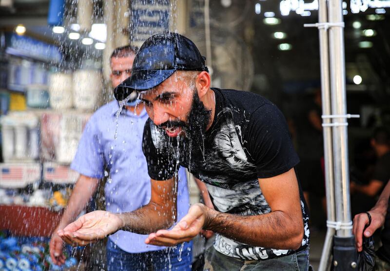 A man stands under a roadside shower along Sinak Street in Baghdad to cool off during a heatwave in Iraq. AFP