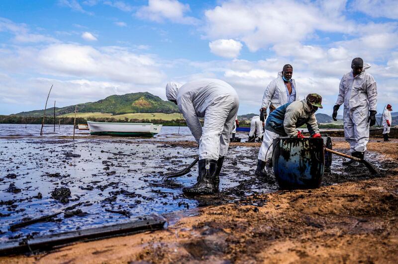 TOPSHOT - People scoop leaked oil from the vessel MV Wakashio, belonging to a Japanese company but Panamanian-flagged, that ran aground and caused oil leakage near Blue bay Marine Park in southeast Mauritius on August 9, 2020. France on August 8, 2020 dispatched aircraft and technical advisers from Reunion to Mauritius after the prime minister appealed for urgent assistance to contain a worsening oil spill polluting the island nation's famed reefs, lagoons and oceans. Rough seas have hampered efforts to stop fuel leaking from the bulk carrier MV Wakashio, which ran aground two weeks ago, and is staining pristine waters in an ecologically protected marine area off the south-east coast. / AFP / L'Express Maurice / Daren Mauree
