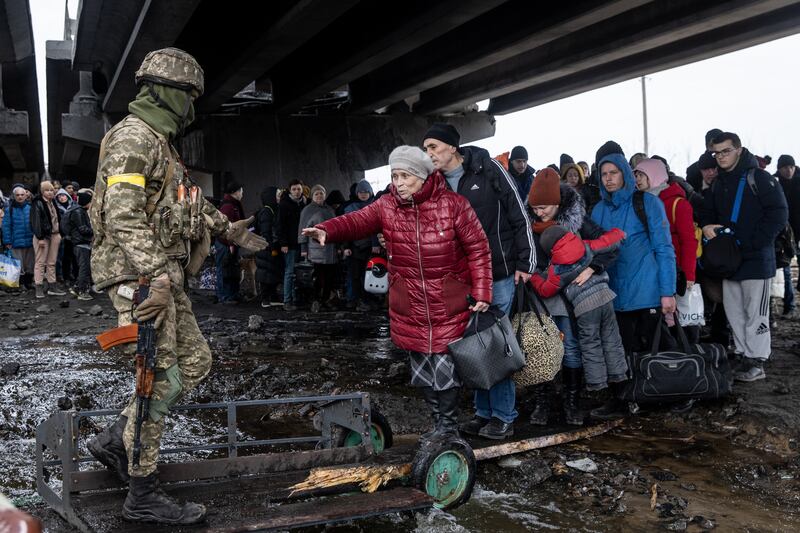 Soldiers assist Irpin residents underneath a damaged bridge as they flee. Getty
