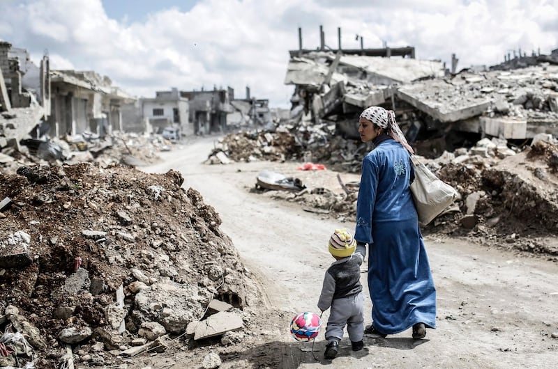 A Kurdish Syrian woman walks with her child past the ruins of the town of Kobane, also known as Ain al-Arab. AFP