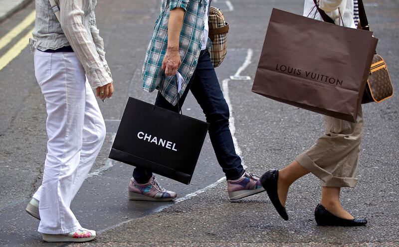 Customers carry branded shopping bags from Chanel SA, and LVMH Moet Hennessy Louis Vuitton SA stores as they cross Old Bond Street in London, U.K., on Monday, Aug. 15, 2011. U.K. inflation probably accelerated in July as energy costs increased, squeezing Britons who are already facing government spending cuts and slower economic growth. Photographer: Simon Dawson/Bloomberg