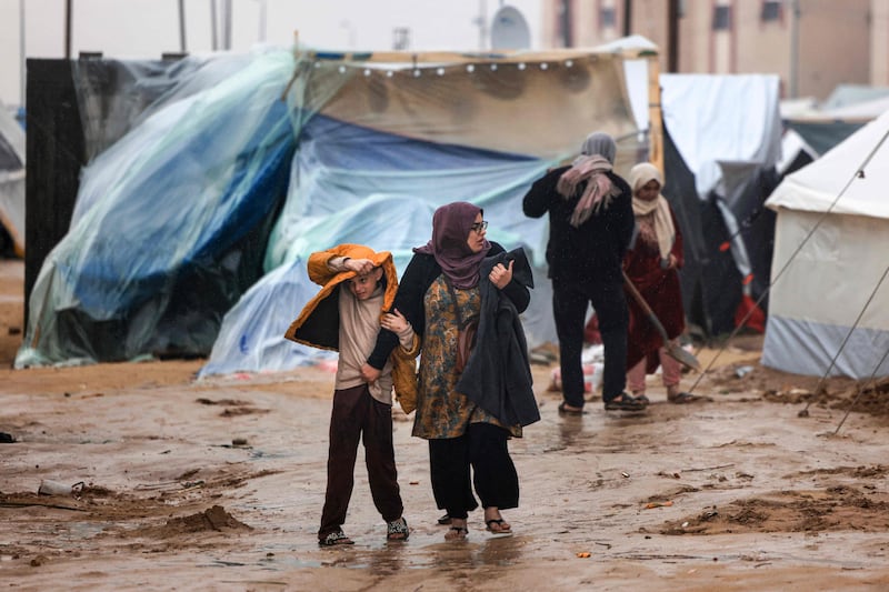 Palestinians walk in the rain at a camp for displaced people in Rafah, southern Gaza Strip. AFP