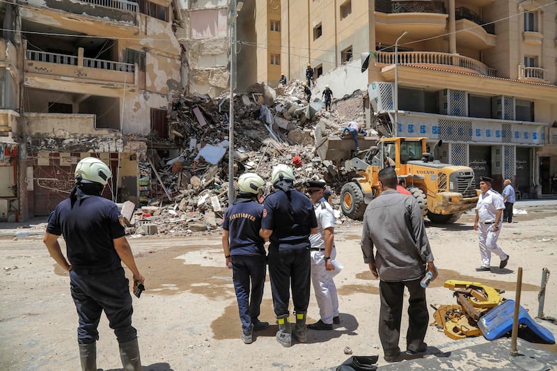 Civil defence first responders speak with a policeman (white) at the scene of a collapsed 13-storey-building in the Sidi Bishr district of Egypt's northern city of Alexandria on June 26, 2023.  (Photo by Hazem GOUDA  /  AFP)